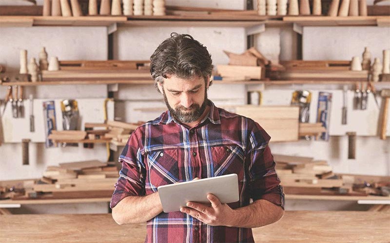 Handwerker im Holzlager nutzt Tablet zur Planung von Werkstattprojekten