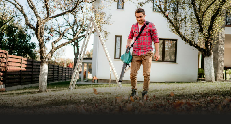 Mann verwendet Laubbläser im Garten zur Reinigung von Herbstlaub